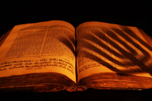 Eski İbrani İncili, arka planda yanan mum ışığında. Karanlıkta açık Yahudi dua kitabının üzerindeki menorah 'ın gölgesi. Yakın çekim.