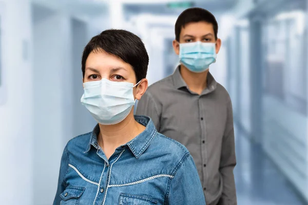Hastane veya tıp merkezinde koruyucu maske takan iki kişi. Orta yaşlı beyaz bir kadın ve maskeli genç bir çocuk. COVID-19 salgını önleme. Coronavirüs salgını konsepti