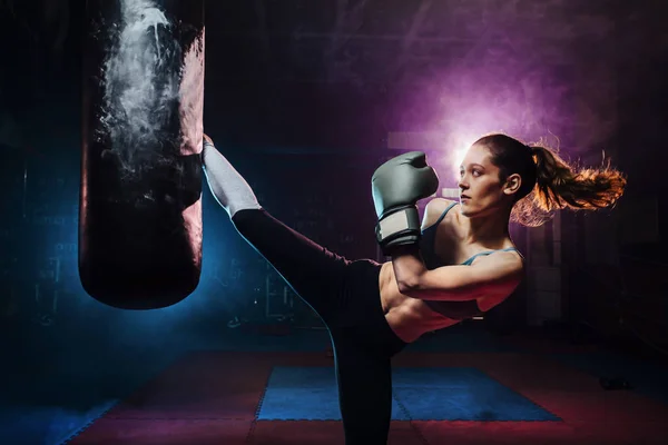 Mujer joven de entrenamiento de autodefensa dando una patada alta a la bolsa de boxeo concepto de boxeo, autodefensa, entrenamiento — Foto de Stock