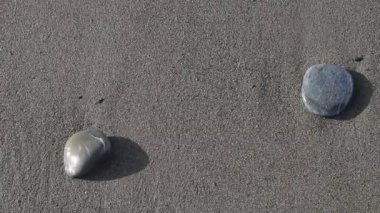 Köpüklü deniz dalgası kumsalda çakıl taşlarını yıkar.