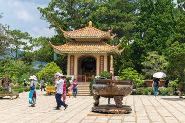Dalat, Vietnam - 15 Nisan 2019: Turistler parktaki eski bir kilisenin yanında tropikal bir ülkede büyük metal vazoyla yürüyorlar