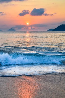 Waves on the seashore and sun from the clouds at dawn with reflection in water