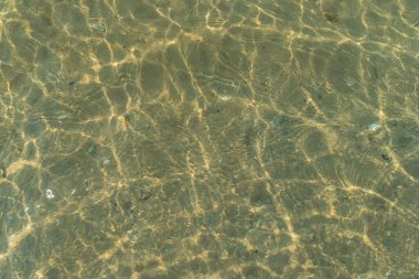 Çakıl taşları ve su yüzeyindeki dalgaların yansımasıyla kumlu taban.