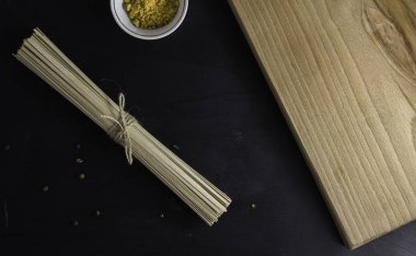 soba - karabuğday eriştesi (çiğ karabuğday eriştesi). Koyu arkaplanda tahta bir kesme tahtasının üzerinde, iple bağlanmış baharatlı makarna..
