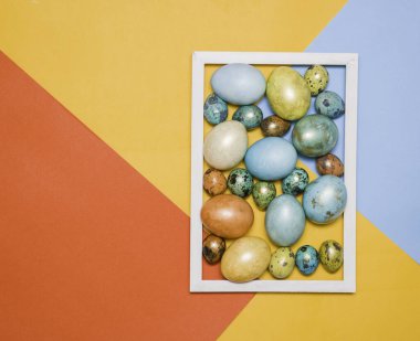 Renkli arka planda ahşap beyaz çerçeveli renkli Paskalya yumurtaları. Metin için boş alan. Mutlu Paskalyalar!