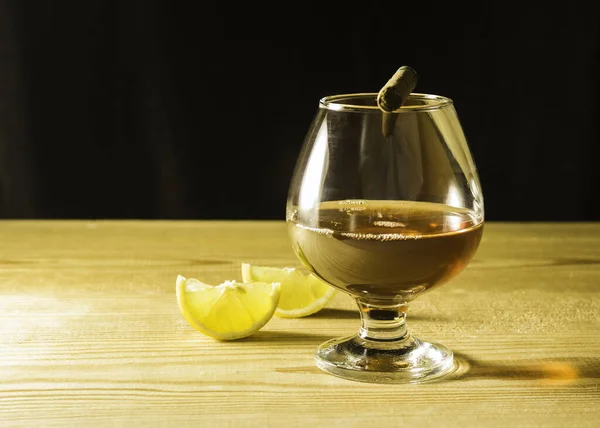 木製のテーブルの上にコニャックのガラス レモンとガラス上のシガーのスライス 横のテキストのためのフリースペース — ストック写真