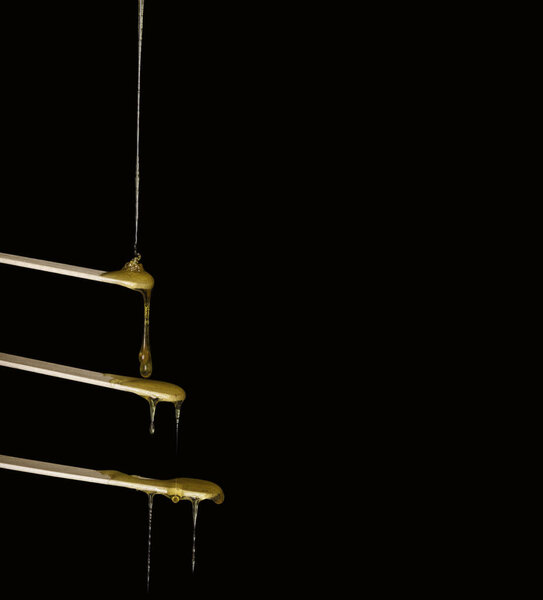 The sugar paste or wax shugaring beauty flows down to the wooden tongue depressors, lot of boards to wax. Black background, free space for text.