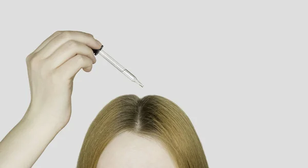 A glass pipette with a hair growth agent is applied to the parting of the hair, red hair. Hair care. Light background, free space for text.