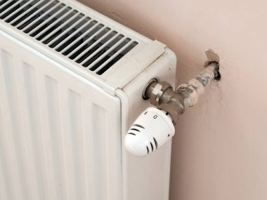 thermostat on old white radiator on pink wall background