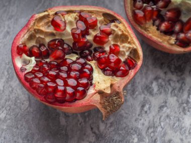 sliced ripe pomegranate with fruit kernels close up on a gray stone