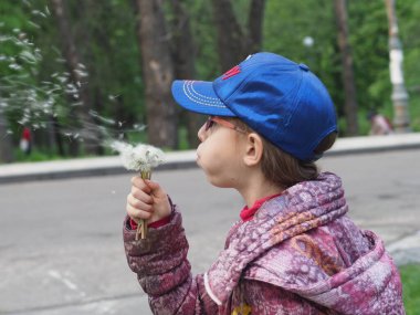 Karantina sırasında gözlüklü, kot şapkalı ve tıbbi maskeli Avrupalı bir kız karahindiba tohumları saçar.