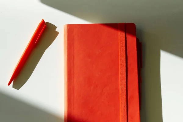 Kırmızı defter kalem güneş ışığı beyaz masa — Stok fotoğraf