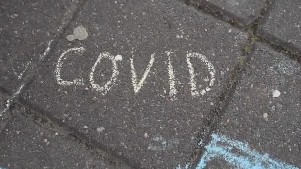 La main des enfants efface l'inscription à la craie rouge covide sur les carreaux d'asphalte — Video