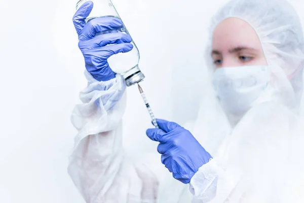 Un virologo con una tuta antivirale e una maschera medica riempie una siringa di medicinale rosa. Un'infermiera con una siringa in mano su uno sfondo bianco . — Foto Stock