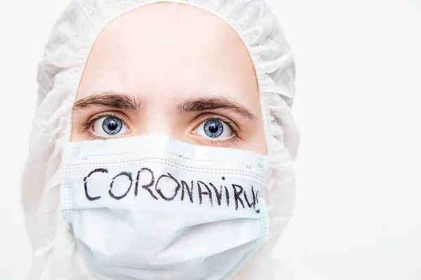 Beyaz maskeli ve viral koruyucu giysili mavi lastik eldivenli bir virüs uzmanı kameraya korkunç bir şekilde bakıyor ve koronavirüs salgınını nasıl durduracağını ve ne yapacağını düşünüyor. Gözlerindeki korku....