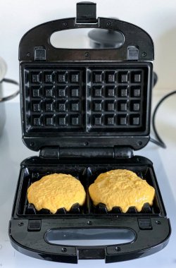 Beyaz bir masada siyah bir waffle ızgarasında Belçika waffle 'ı pişirmek.