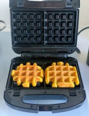 Beyaz bir masada siyah bir waffle ızgarasında Belçika waffle 'ı pişirmek.