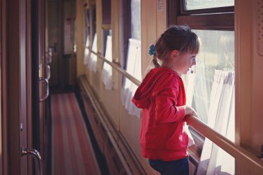 5 yaşında bir kız, trenin camından dışarı bakıyor.