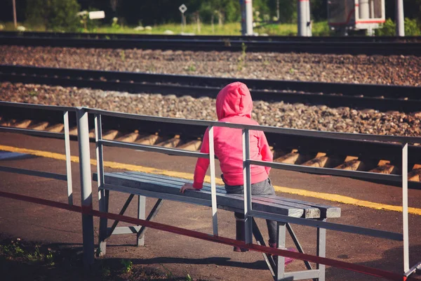 Demiryolunun kenarındaki bankta oturan beş yaşında bir çocuk.