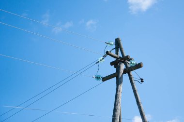 Mavi gökyüzüne karşı elektrik kabloları olan eski elektrik direği