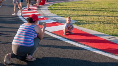Mogyorod Macaristan 08 01 01 2019: Anne, oğlunun Motor Yarış Pistinin kırmızı ve beyaz kaldırımlarında fotoğraflarını çekiyor.