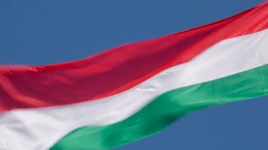 Macaristan ulusal bayrağı mavi arka planda rüzgarda dalgalanıyor. Macaristan Cumhuriyeti bayrağı gökyüzünde dalgalanıyor..
