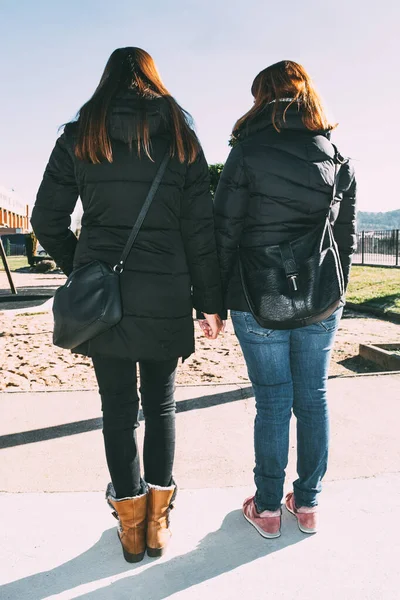 Two girls holding hands watching a playground on a sunny winter\'s afternoon
