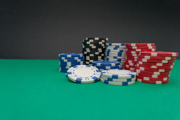 Fichas de casino blancas, negras, azules y rojas, apiladas sobre un fondo verde — Foto de Stock