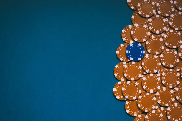 Stack of yellow poker chips and a blue chip on top on a blue board