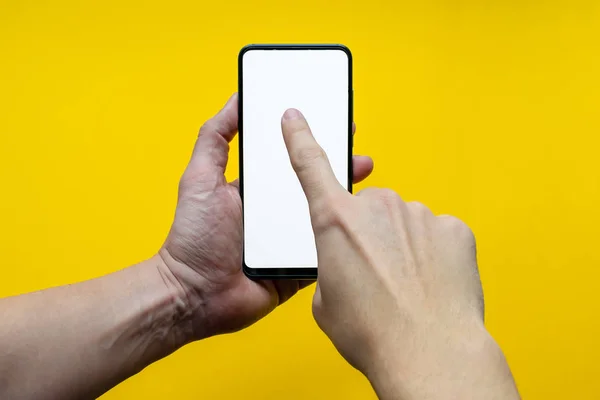 Erkek el ele tutuşup, sarı arka planda izole edilmiş, dik bir şekilde boş siyah smatphone ekranına dokunuyor. Model için boş ekran
