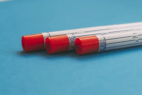 Three laboratory sample tubes with red cap on blue background. Medical tests