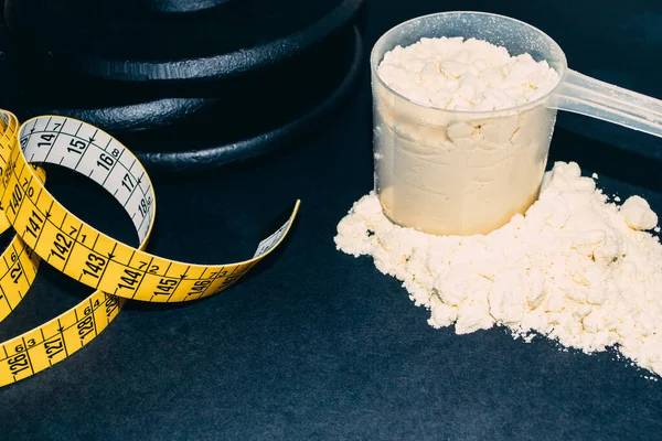 Beyaz Protein kaşık tozu yakın çekim, ağırlıklar ve mezura ile. Spor beslenmesi 