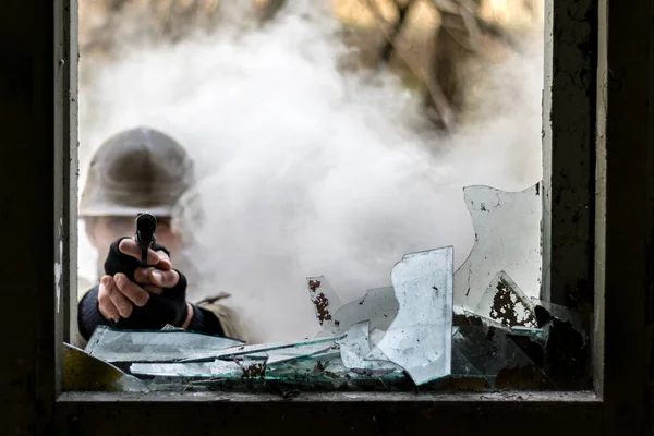 Photo of a solder pointing a gun trough a window while there is fog outside