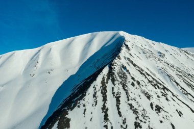 Güneşli bir havada karla kaplı dağların yamaçlarında.