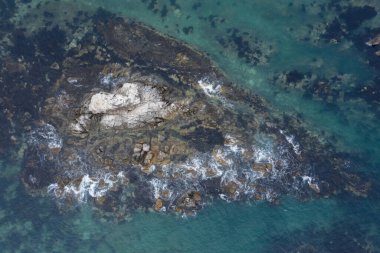 Deniz suyu kıyı taşlarında dalgalanır ve onlara karşı kırılır..