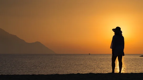 Mulher de pé e assistindo pôr do sol contra o sol — Fotografia de Stock