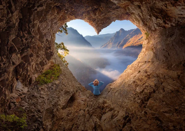 Frau in herzförmiger Höhle beobachtet die neblige Schlucht am Morgen — Stockfoto