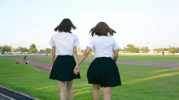 Deux mignon asiatique thaïlandais collège étudiant fille en uniforme universitaire marcher dans la scène tenant la main en jouant avec plaisir et joie dans heureux écolière amitié et amour relation concept en HD — Video