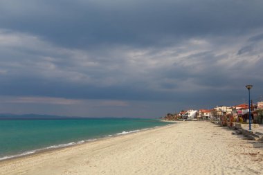 Karanlık bir bulutun altında turkuaz deniz kıyısında köy