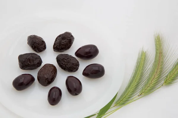 Few dark black olives on a white plate and three green spikes o — Stock Photo, Image