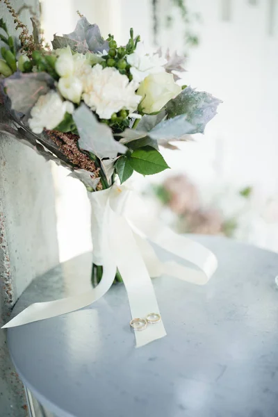 Beautifull wedding bouquet with roses, carnations, white freesia in cream tones with gold wedding rings on the ribbon.