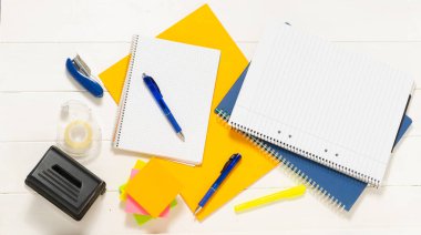 Kalem ve çıkartmalı not defteri. Not defteri, kalem, kitap ve kalem tutacağı beyaz tahta masanın üzerinde ayakkabı şeklinde. Metin için yer.