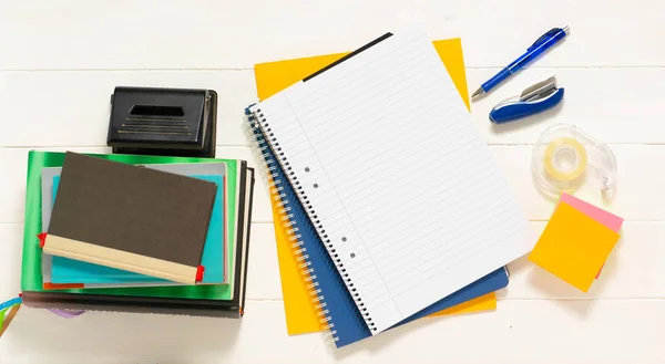 Notepad with pens and stickers. Notebook, pen, books, and pencil holder in the shape of shoe on the white wooden table. Place for text.