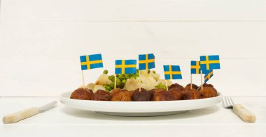 Geleneksel İsveç köfteleri (kottbullar) beyaz tabakta karnabahar ve yeşil bezelye ile. İsveç bayrakları. İsveç ulusal gıda konsepti. Mesaj atmak için arka plan fotoğrafı. Yan görünüm.