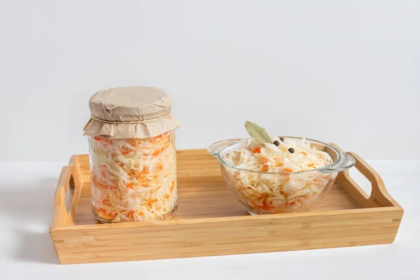 Homemade sauerkraut. Fermented food. Sauerkraut with carrots in a glass jar and bowl in a wooden tray on a white background