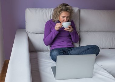 bir fincan kahve laptop önünde kanepede oturan genç kadınla