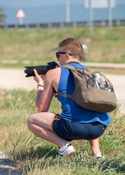 Young man squatting with SLR camera — Stock Photo, Image