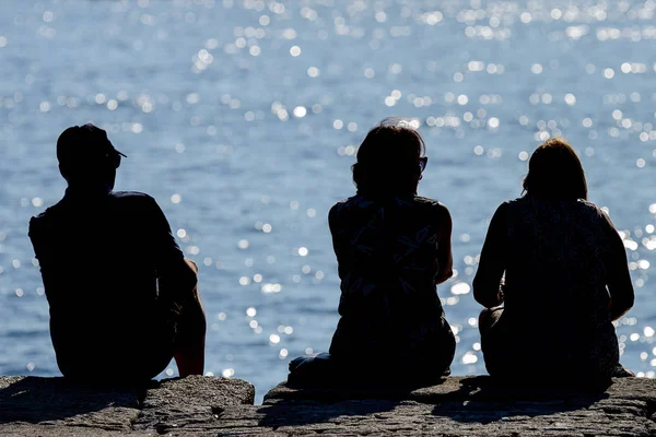 Силуэты мужчины с двумя женщинами, сидящими на пляже и смотрящими на море — стоковое фото
