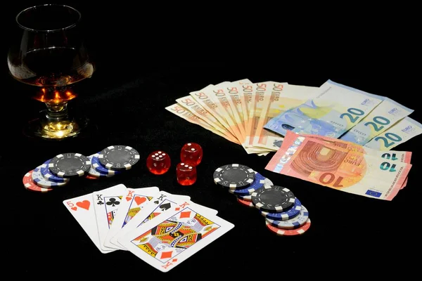 Carte da gioco, patatine fritte, banconote e un bicchiere di cognac su sfondo nero — Foto Stock