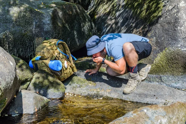 Turist med ryggsäck dricker vatten från en bäck — Stockfoto
